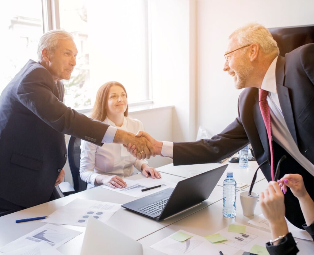 smiling-woman-looking-two-senior-businessman-shaking-hands